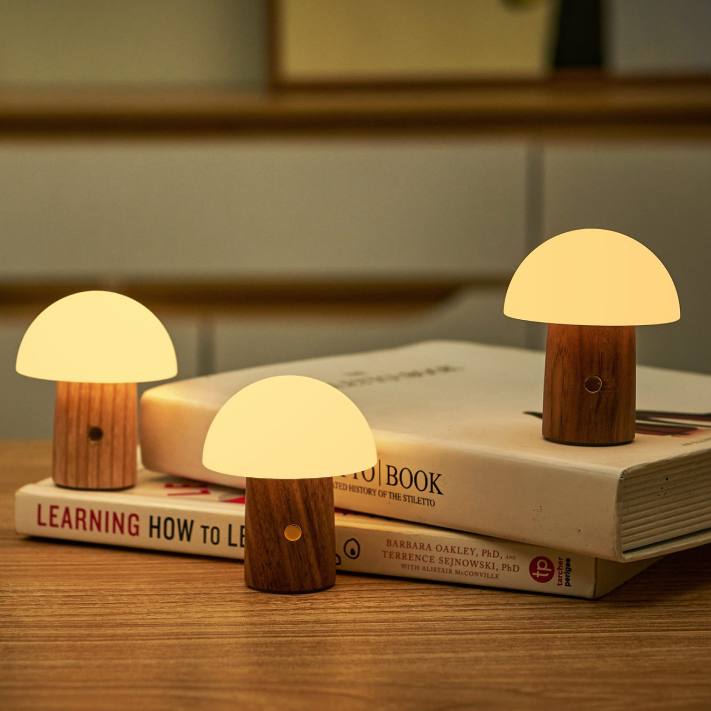 Three mushroom shaped small lights with wooden based placed next to a stack of books.