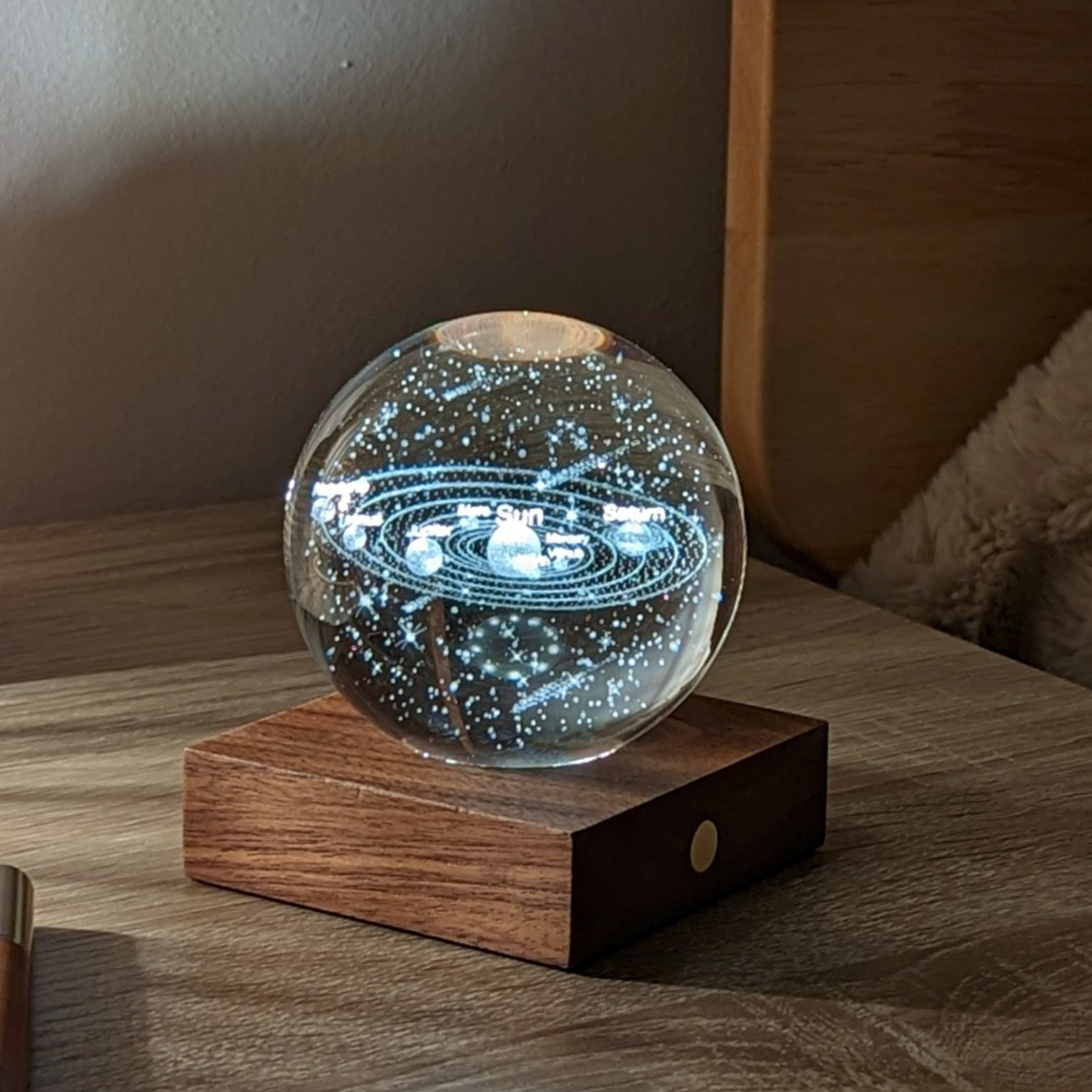 A solar system motif amber crystal light on a walnut wood base, placed on a wooden bedside table.