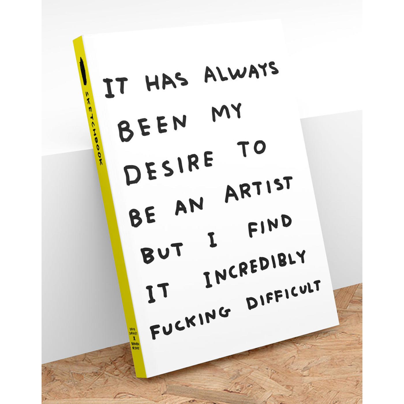 A sketchbook with a white cover featuring black text that reads: 'IT HAS ALWAYS BEEN MY DESIRE TO BE AN ARTIST BUT I FIND IT INCREDIBLY FUCKING DIFFICULT'.