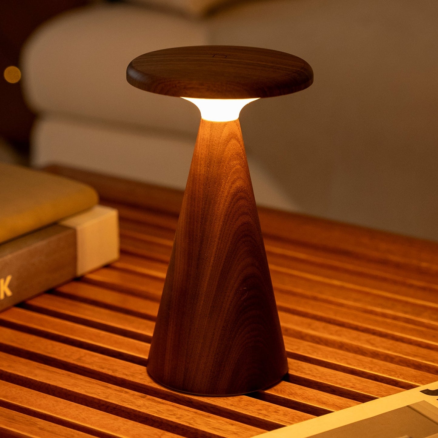 Wooden column shaped lamp on a wooden surface with books in the background