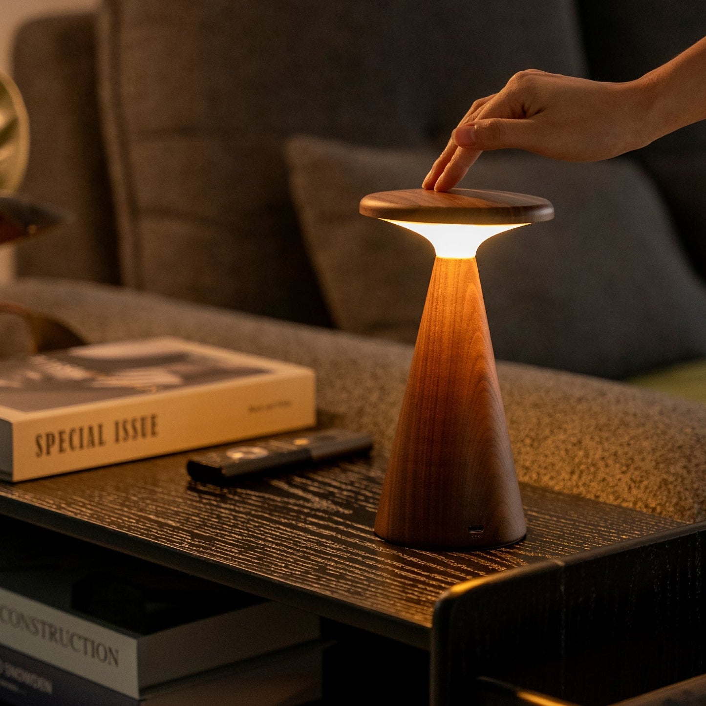 Wooden lamp being adjusted on a table with books and a remote in the background