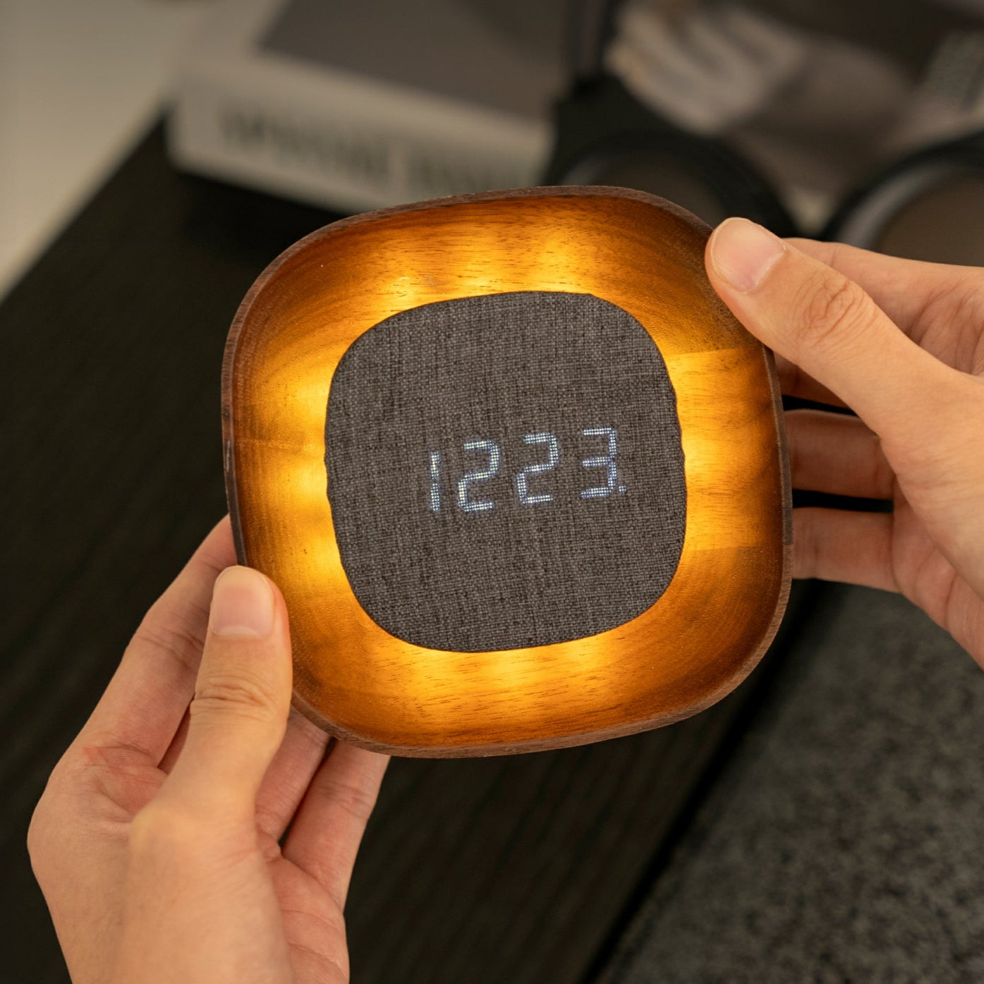 Person holding a square digital clock light with a wooden border and fabric face.