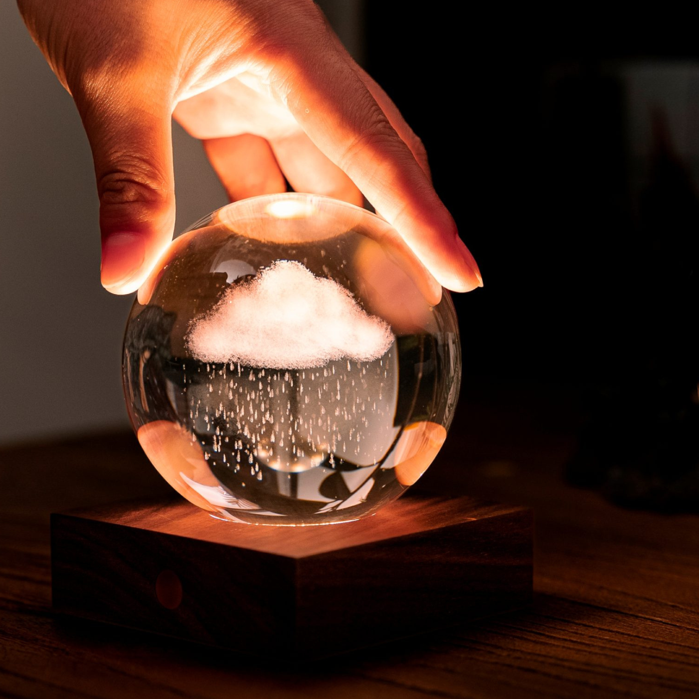 A hand is holding a crystal light globe with a rain cloud motif, illuminated from the inside, displaying a warm light.