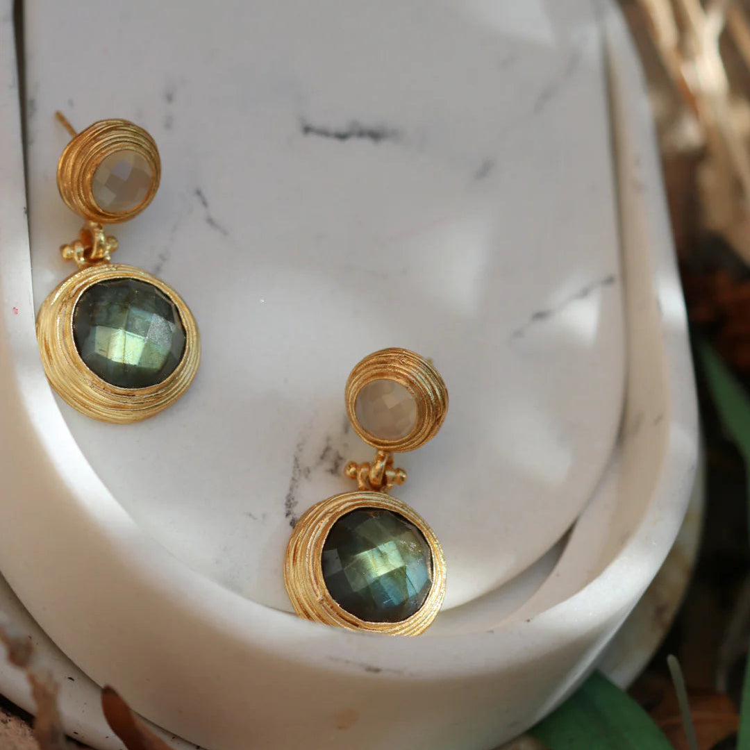 Gold earrings with green gemstones on a white marble surface