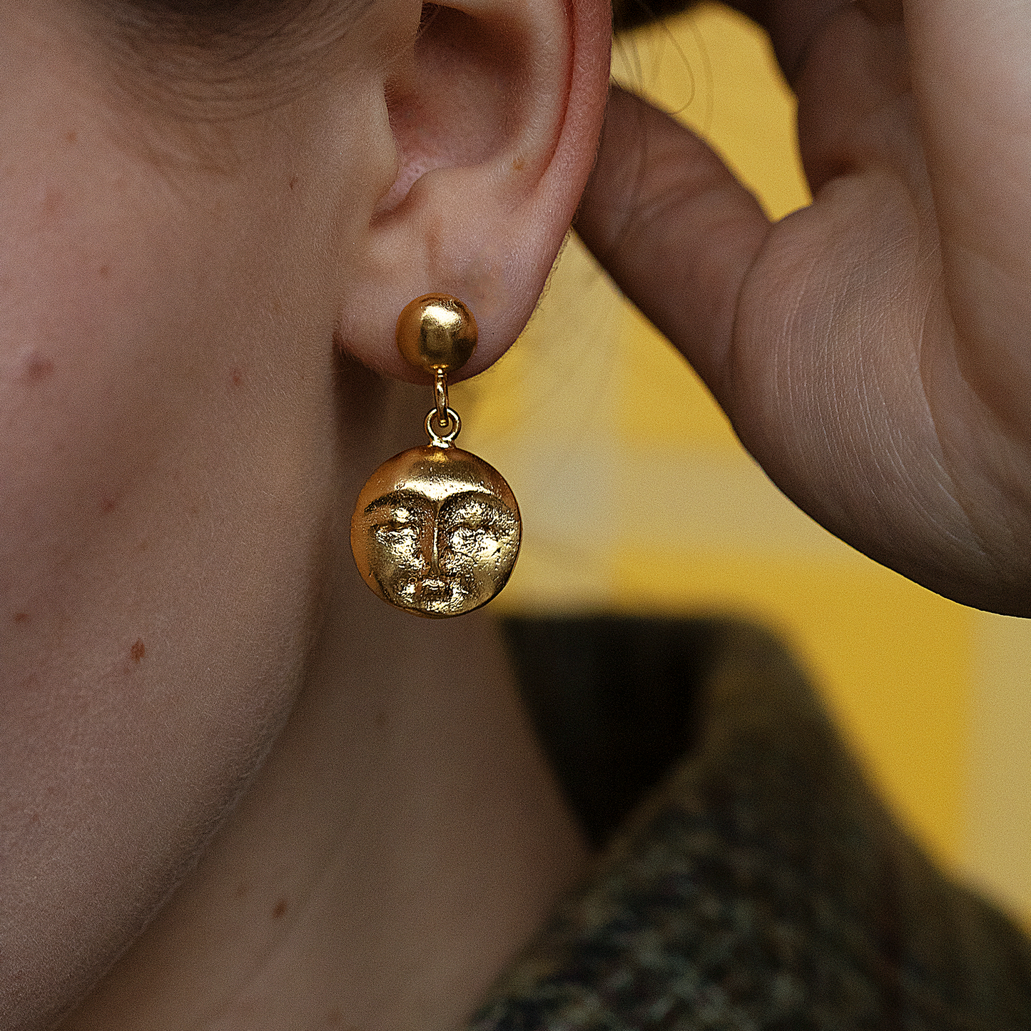 A person wearing a moon face gold drop earring.