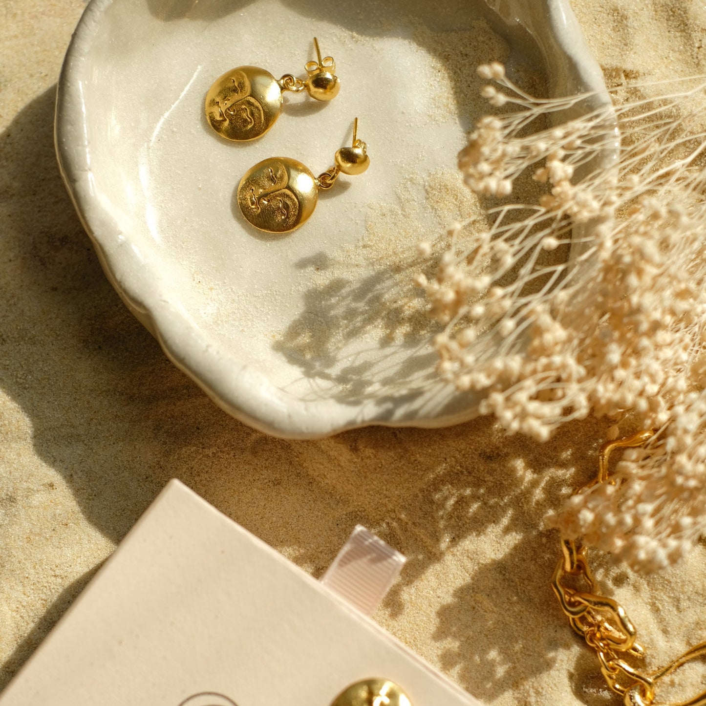 Moon face round gold drop earrings on a ceramic plate.