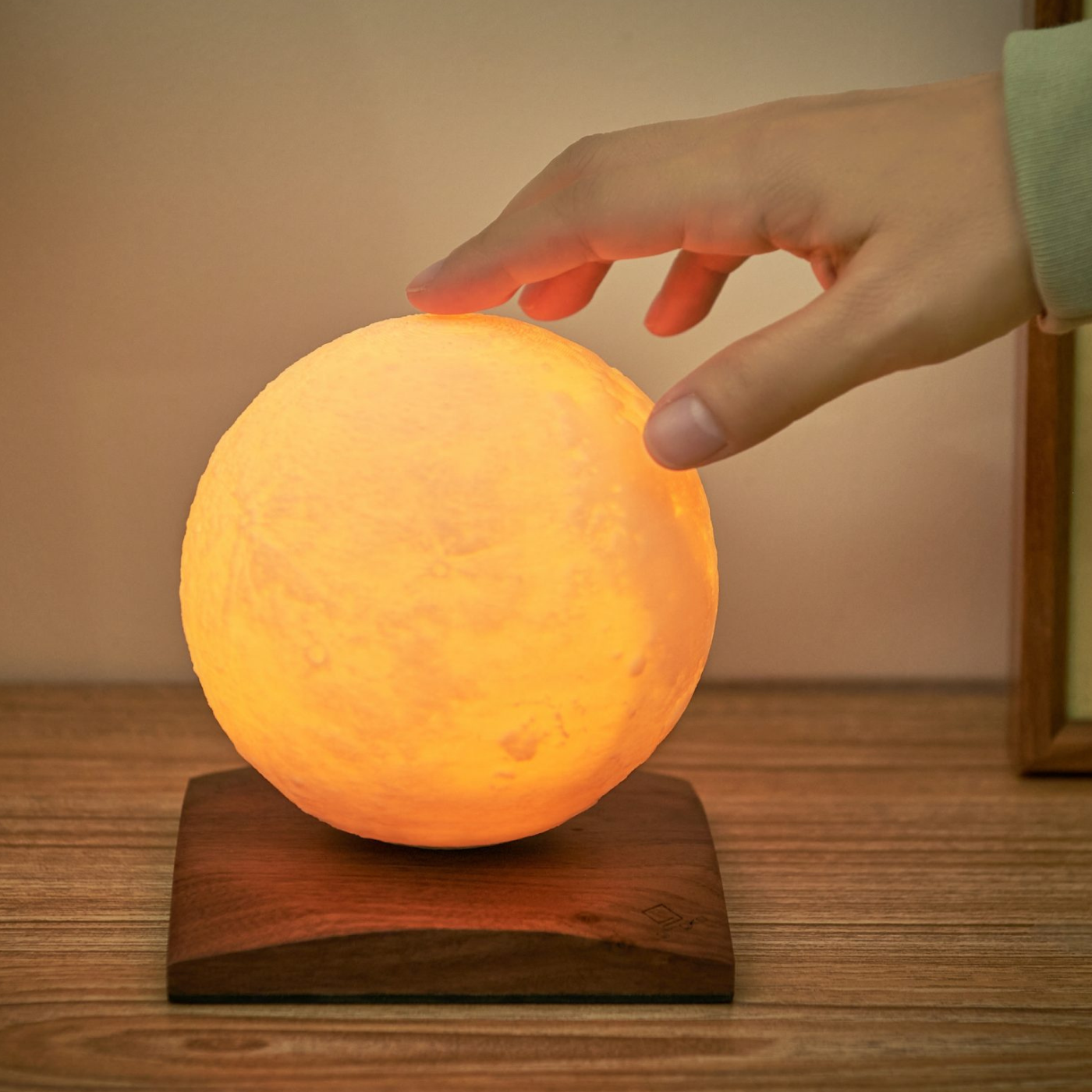 A hand reaching out to a moon shaped light with a warm glow on a wooden base.