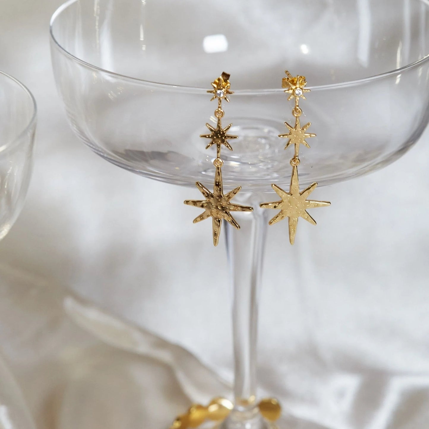 Gold star-shaped earrings on a clear glass with a white background