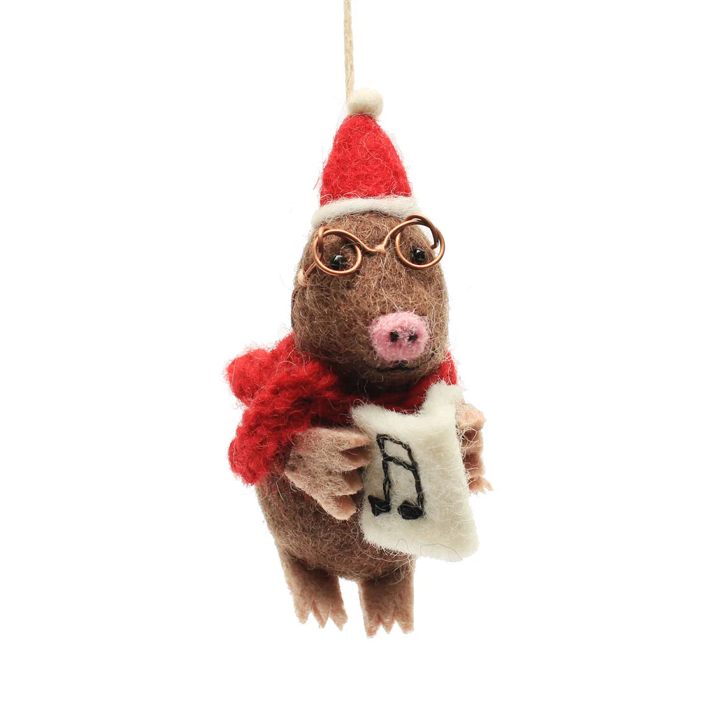 Handmade wool felt mole decoration, with brown body, red scarf, Santa hat, glasses, holding a music sheet, on a white background.