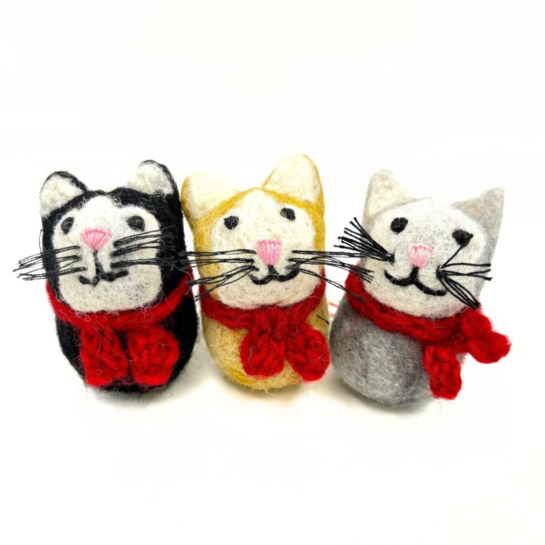 Three cat-shaped Christmas tree ornaments with hand knitted scarves in red, black, and gray colors.