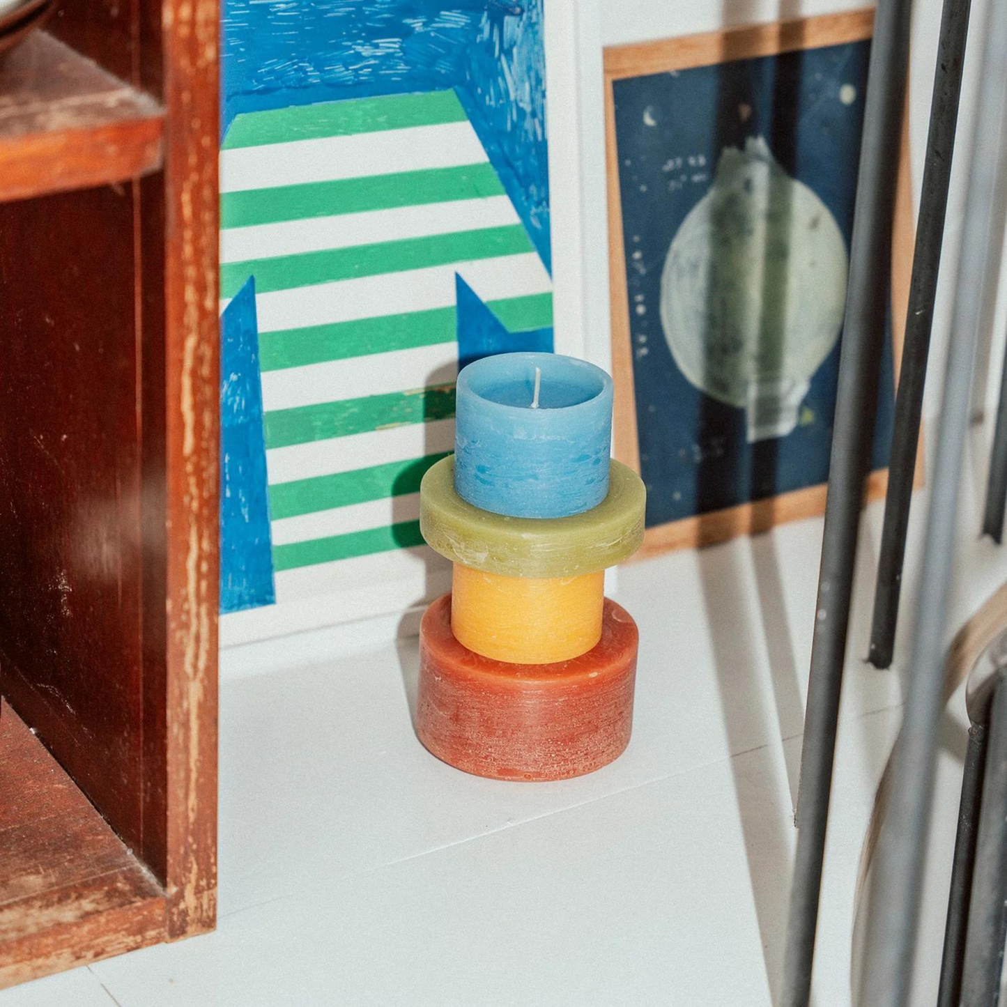 candle made up of 4 different colour components, sitting on the floor against some artwork.
