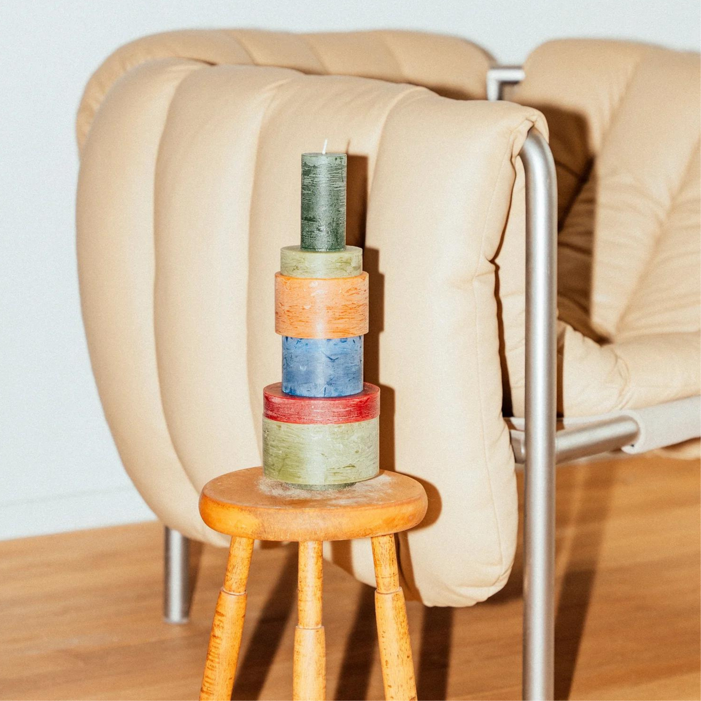  candle made up of 6 different colour components sitting on a stool next to a lounge chair.