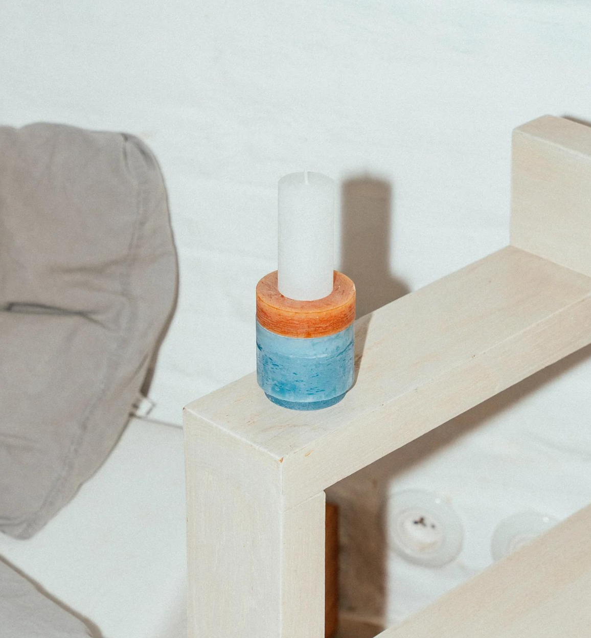 candle made up of 3 different colour components, sitting on an armchair rest.