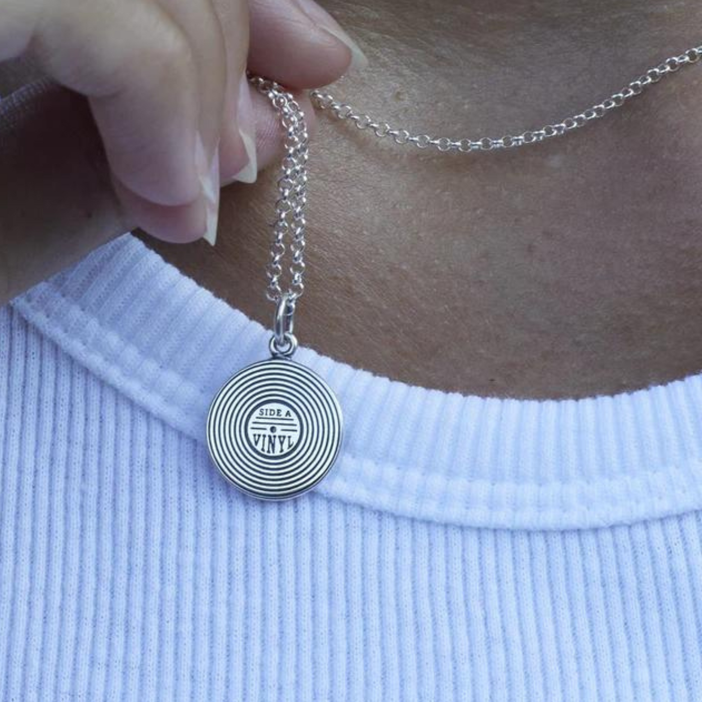 hand holding silver necklace with vinyl charm against neck.