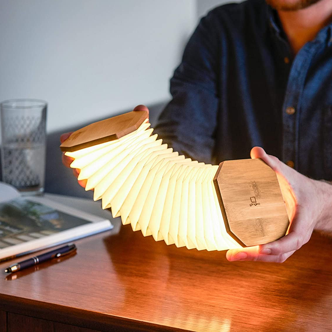 Person holding a wooden, accordion-style lamp on a desk.