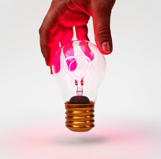A hand holding a lit up cordless heart shaped lightbulb