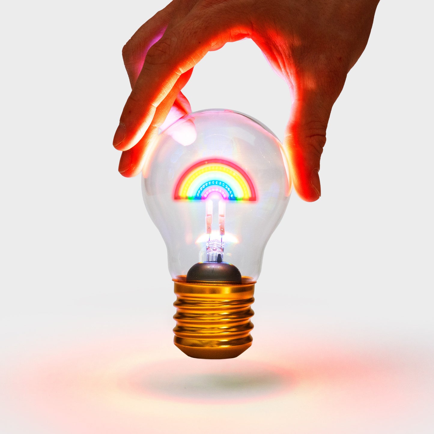 A hand holding a lit up cordless rainbow shaped lightbulb