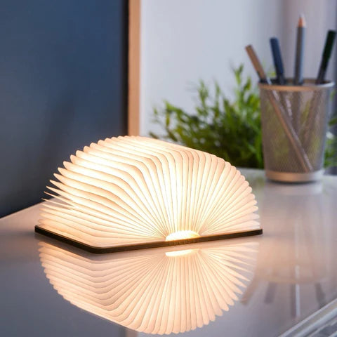 A smart book light resembling a closed wooden book, placed on a table, when opened it emits a soft warm light.