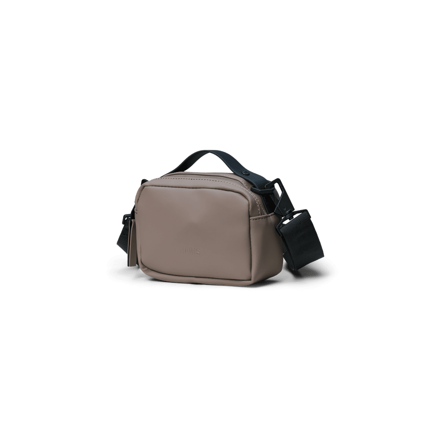 A small rectangular shoulder bag in a muted taupe-beige color with black straps and a matching dark tag, shown against a solid dark green background.