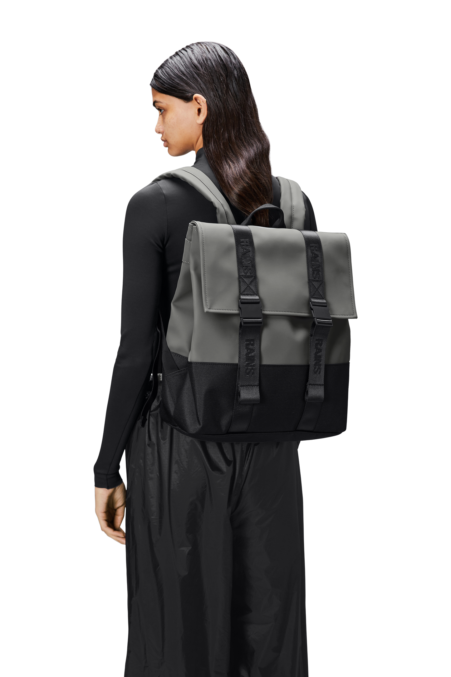 A person wearing black clothes and a square shaped Rains backpack.