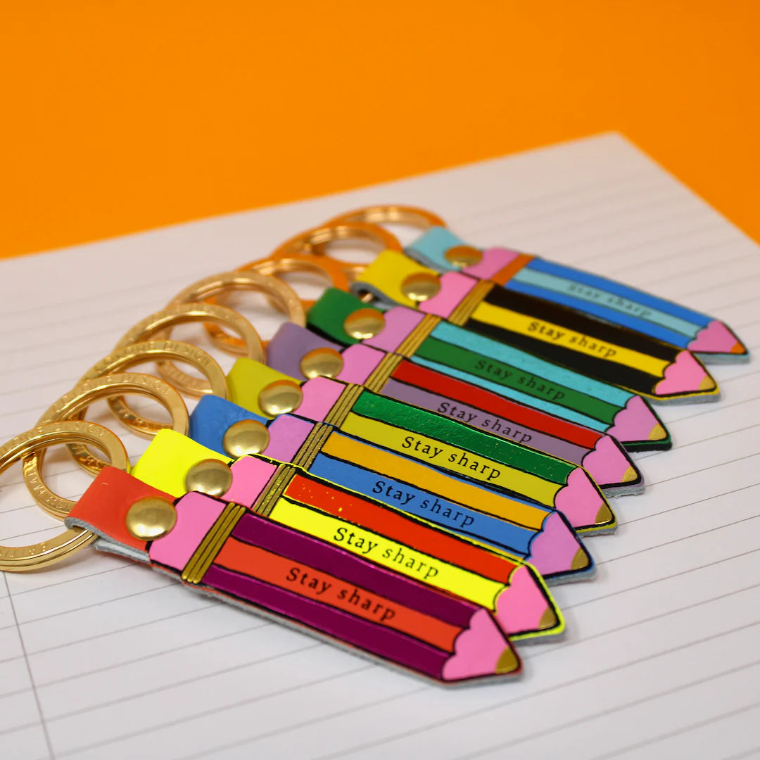 Colorful pencil-shaped keychains with 'Stay sharp' text on a lined paper background.