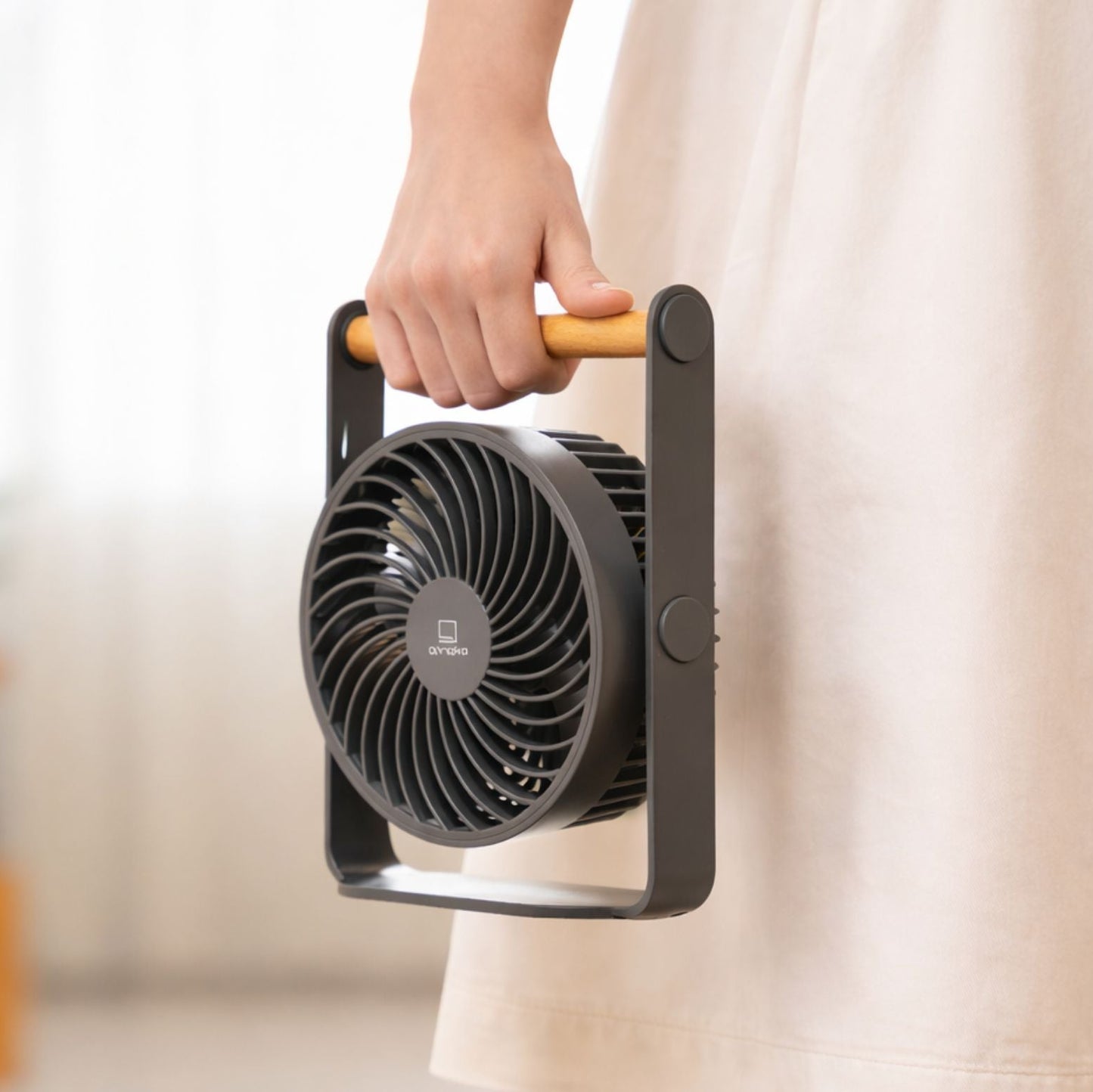 Hand holding a black portable fan with a blurred background