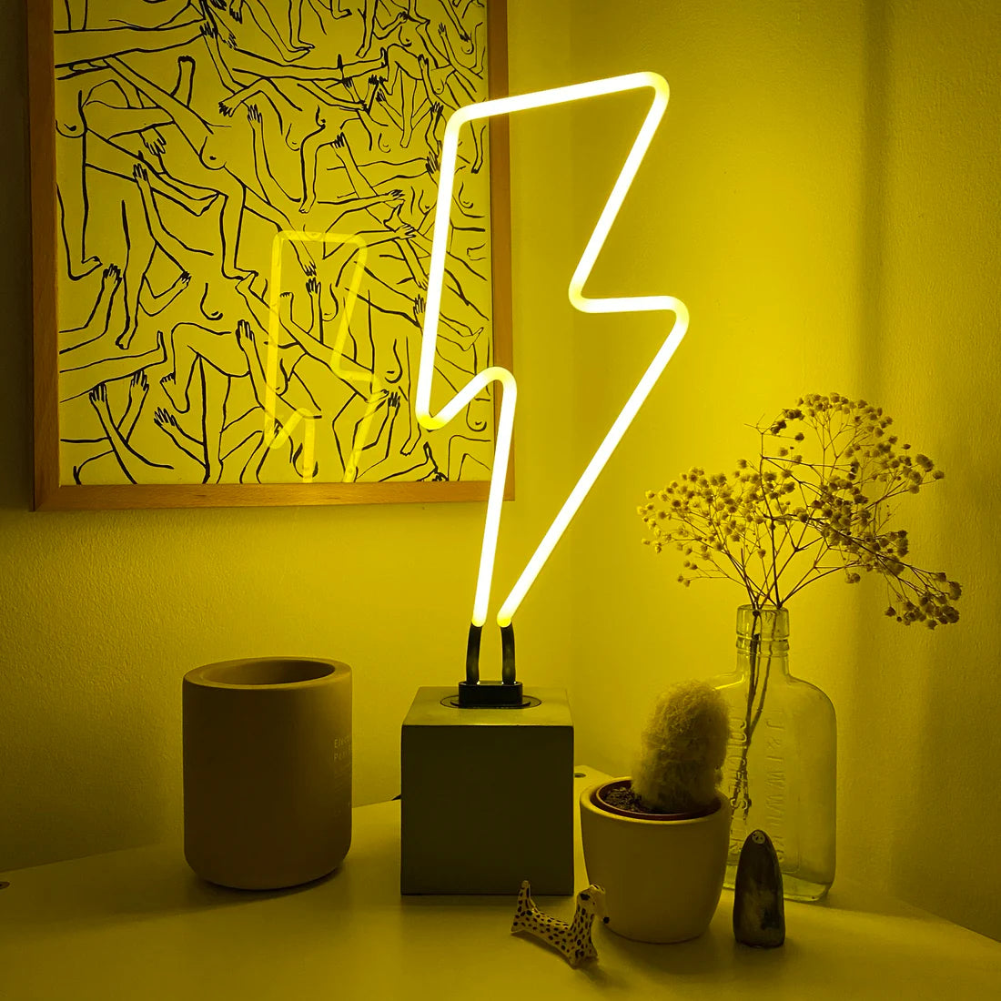 Neon lightning bolt lamp on a table with decorative items against a yellow wall.