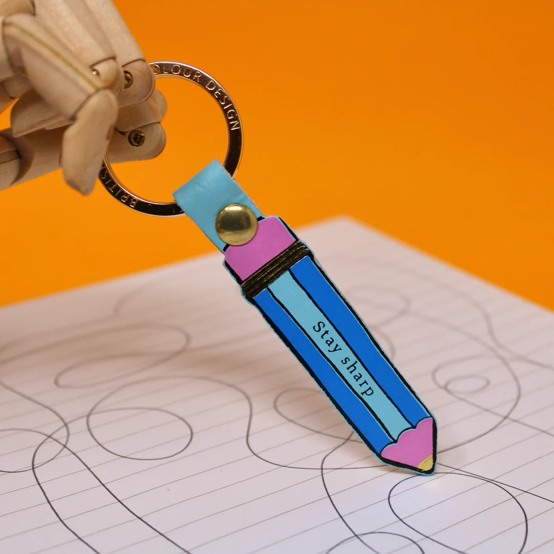 Colorful keychain shaped like a pencil with 'Stay sharp' text on a notebook background
