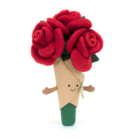 A plush toy resembling a bouquet of red roses with green leaves, wrapped in beige linen with fine cord arms, tied with a ribbon, featuring an embroidered smile.