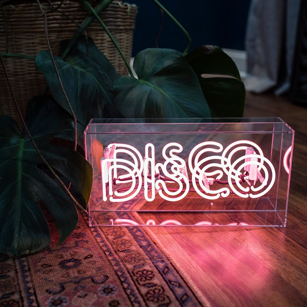 Neon sign with 'DISCO' text on a wooden surface with plants in the background