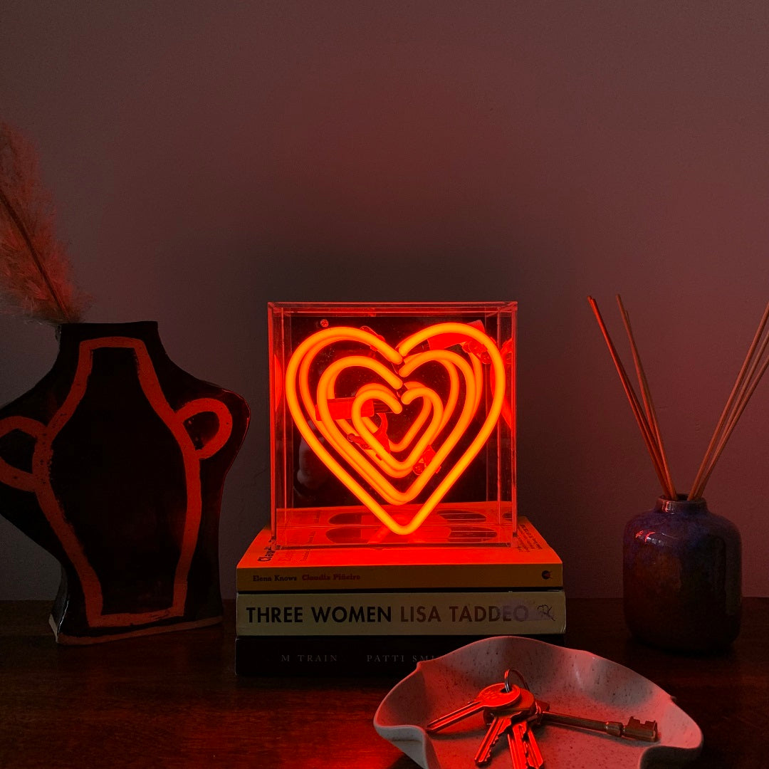 Neon heart light on a stack of books with decorative items on a table.