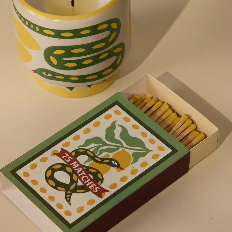 Candle with snake design and a box of matches on a beige surface
