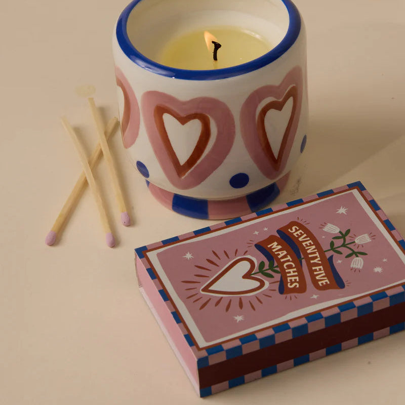 Ceramic candle with heart design, matches, and a matchbox on a beige background