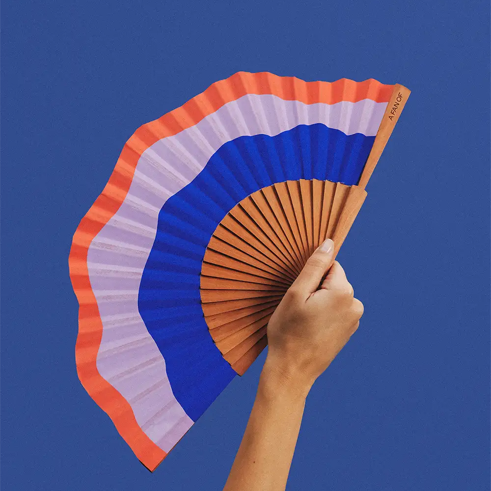Hand holding a colourful fan against a blue background