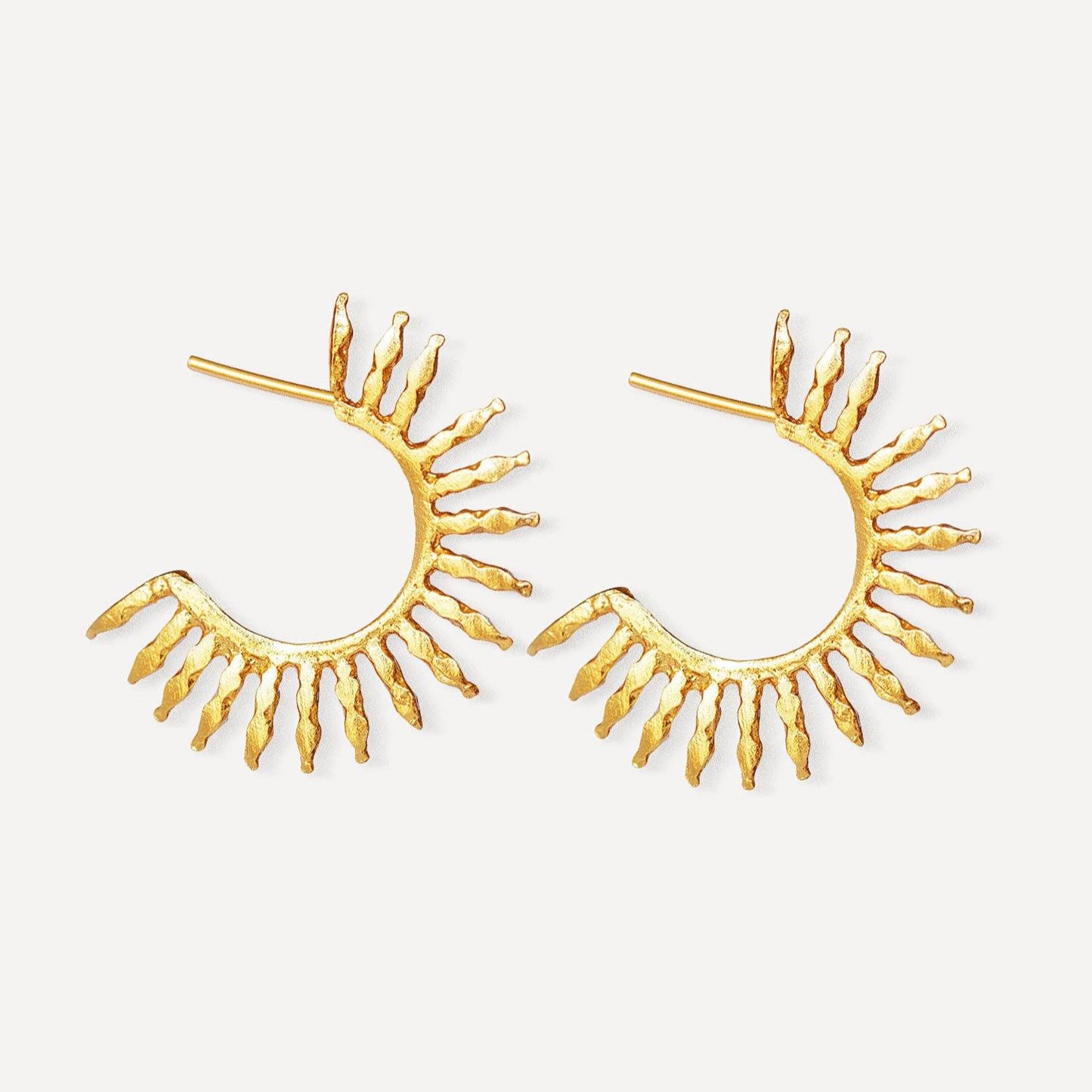 Gold eyelash-shaped hoop earrings on a white background