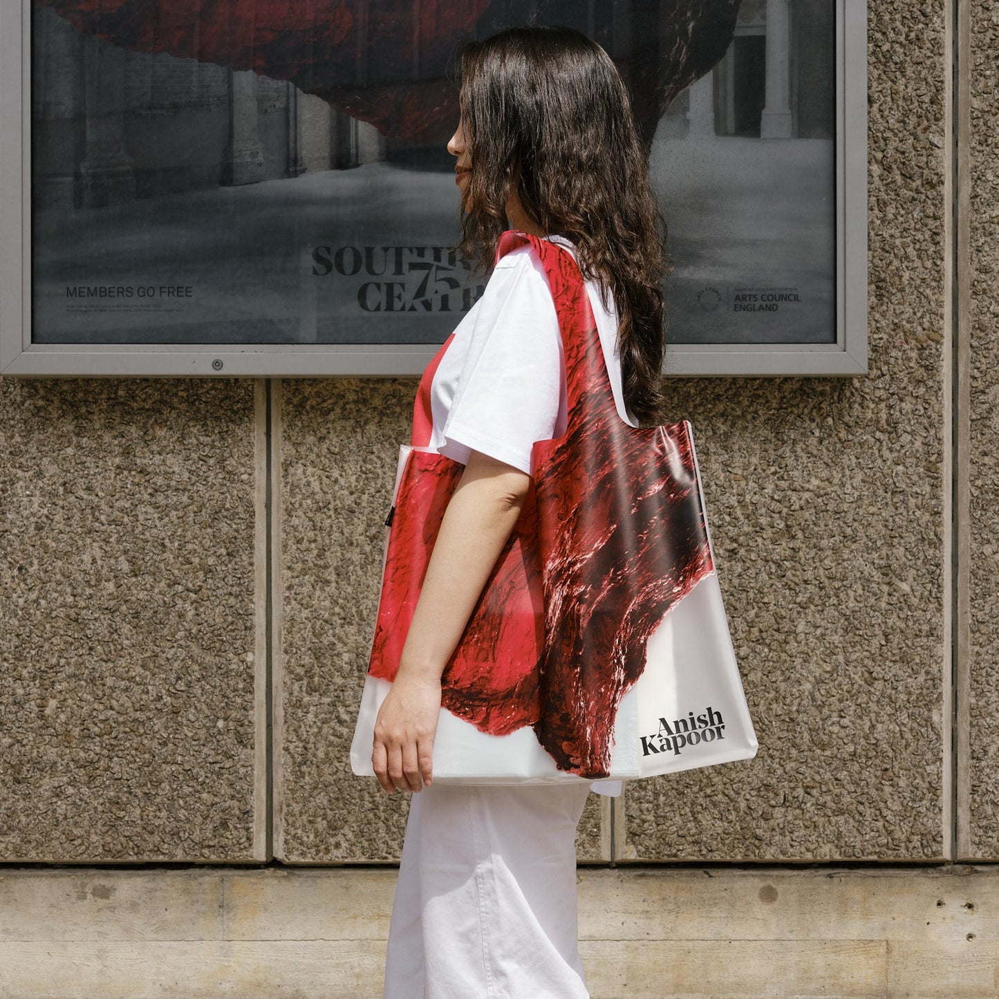 Woman holding a red and white patterned bag in front of a textured wall with a large poster.