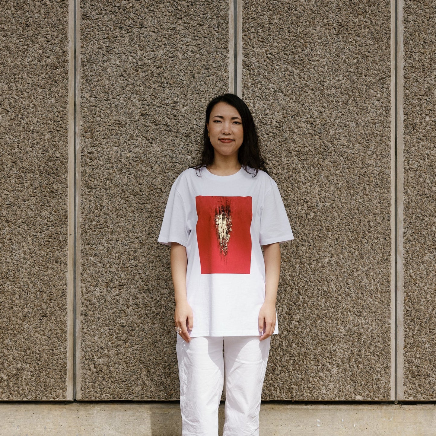 Person wearing a white t-shirt with a red graphic design against a textured wall.