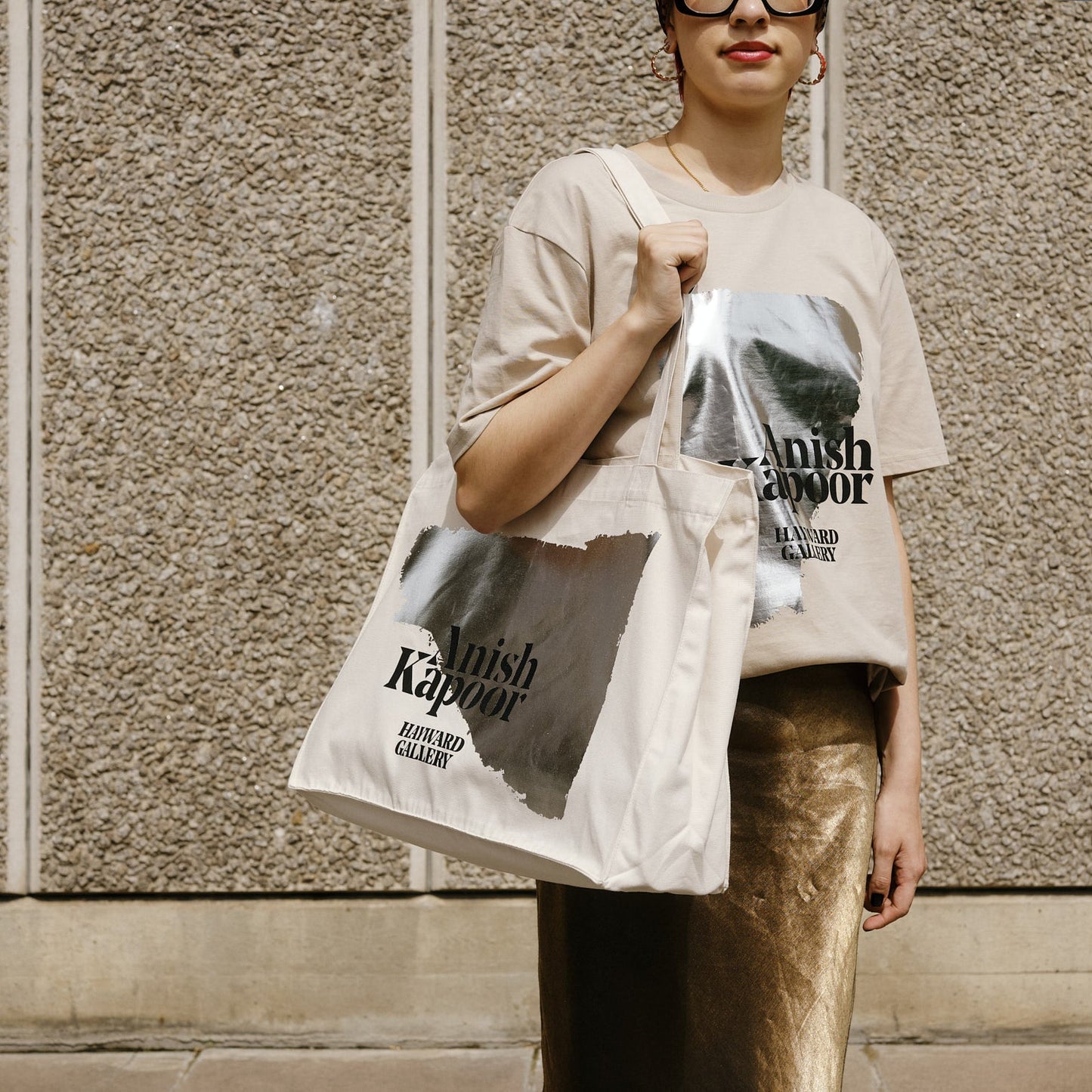 Person holding a branded tote bag against a textured wall