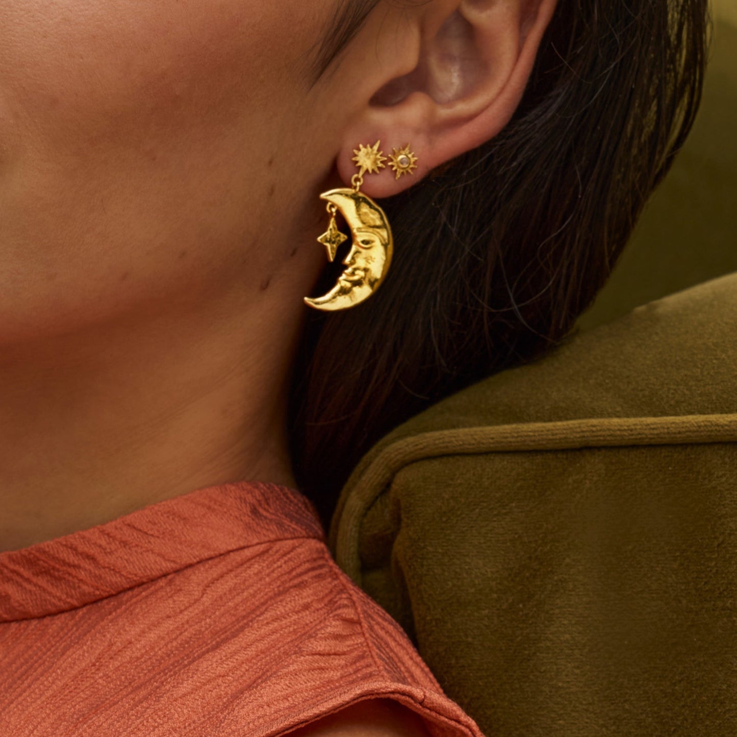 Gold earrings with moon and star designs worn by a person.