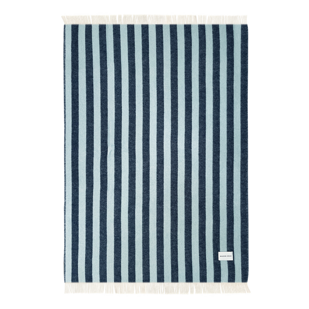 Unfolded wool striped design blanket, with frilly edges and brand label in the right-bottom corner.