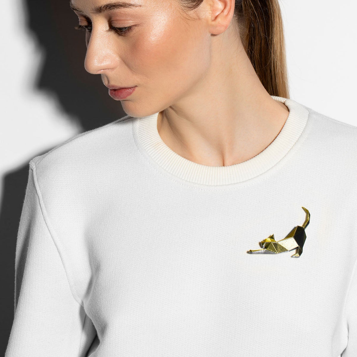 A woman wearing a 3-D printed gold brooch shaped like a cat stretching on a white long sleeve shirt