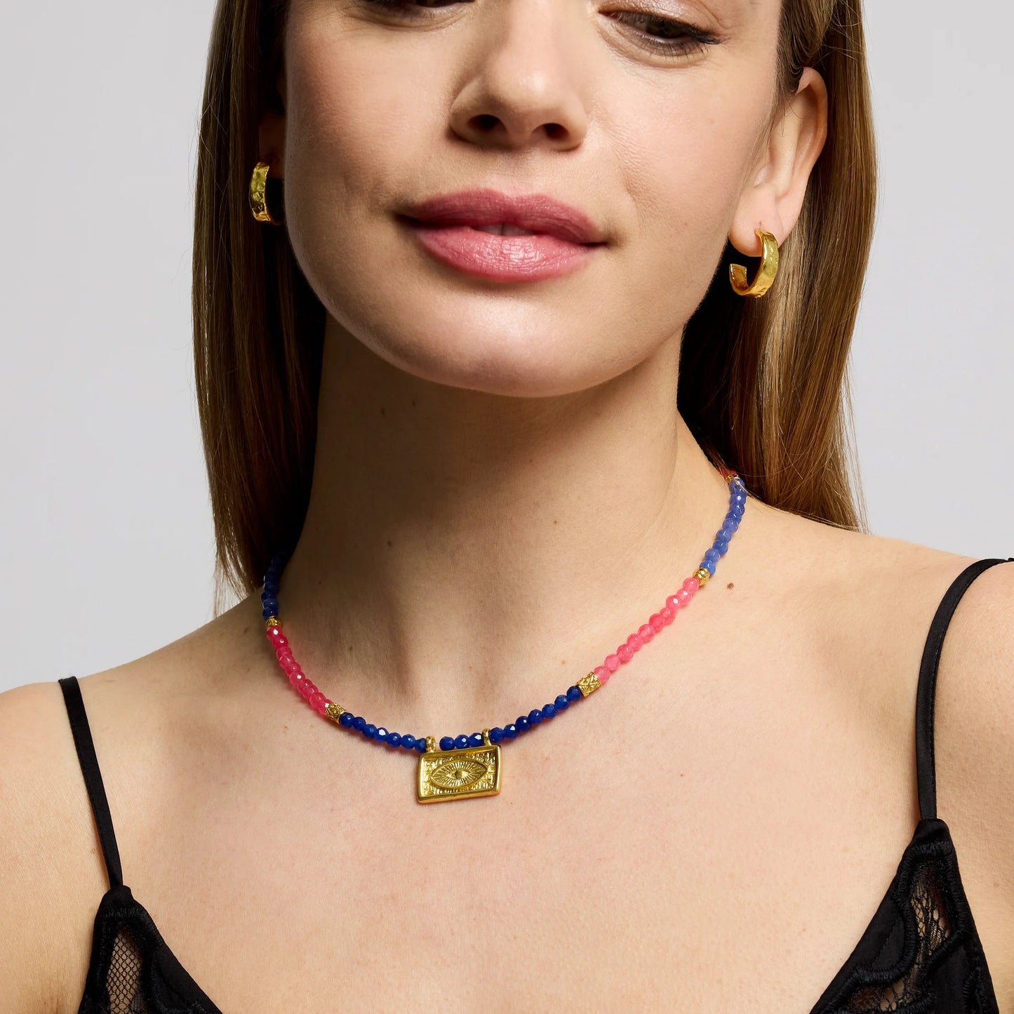 Woman wearing a colorful beaded necklace and gold hoop earrings on a plain background