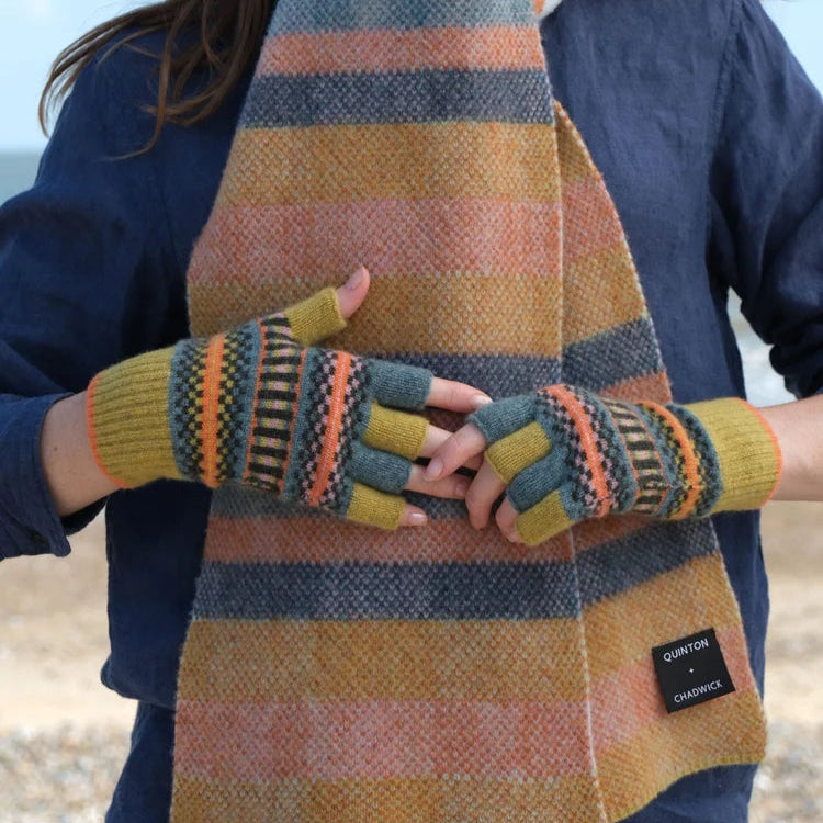 Person wearing a plaid scarf and colorful gloves on a beach