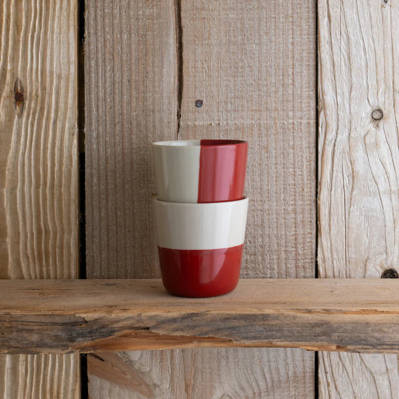 Two ceramic cups with a red and white design stacked on a wooden surface against a wooden background