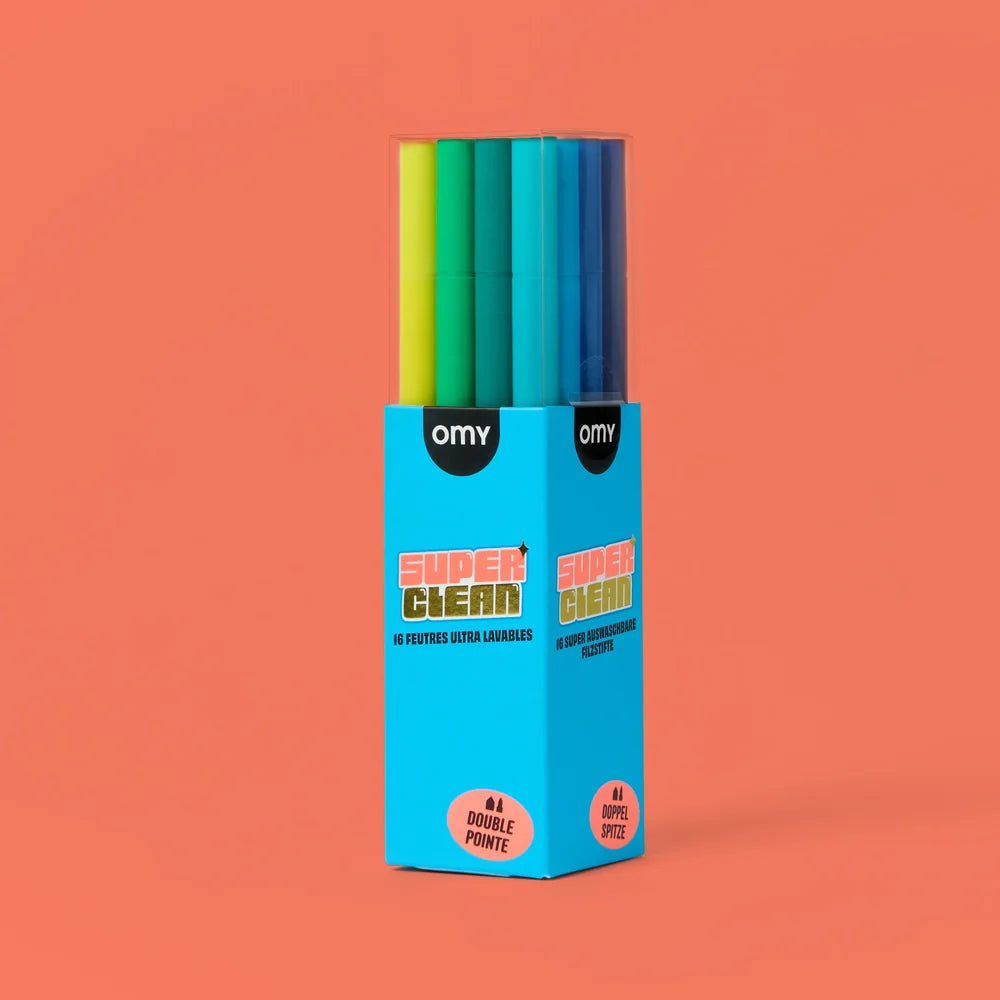 A boxed set of OMY Super Clean double-point marking pens in assorted bright colors, standing upright in a bright blue retail box against a solid coral background.