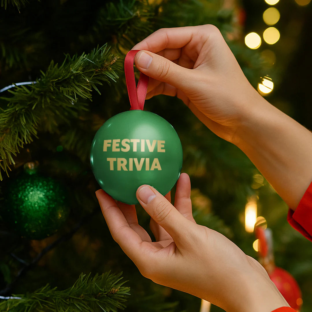 Green ornament with 'Festive Trivia' text being held by a hand against a Christmas tree background.