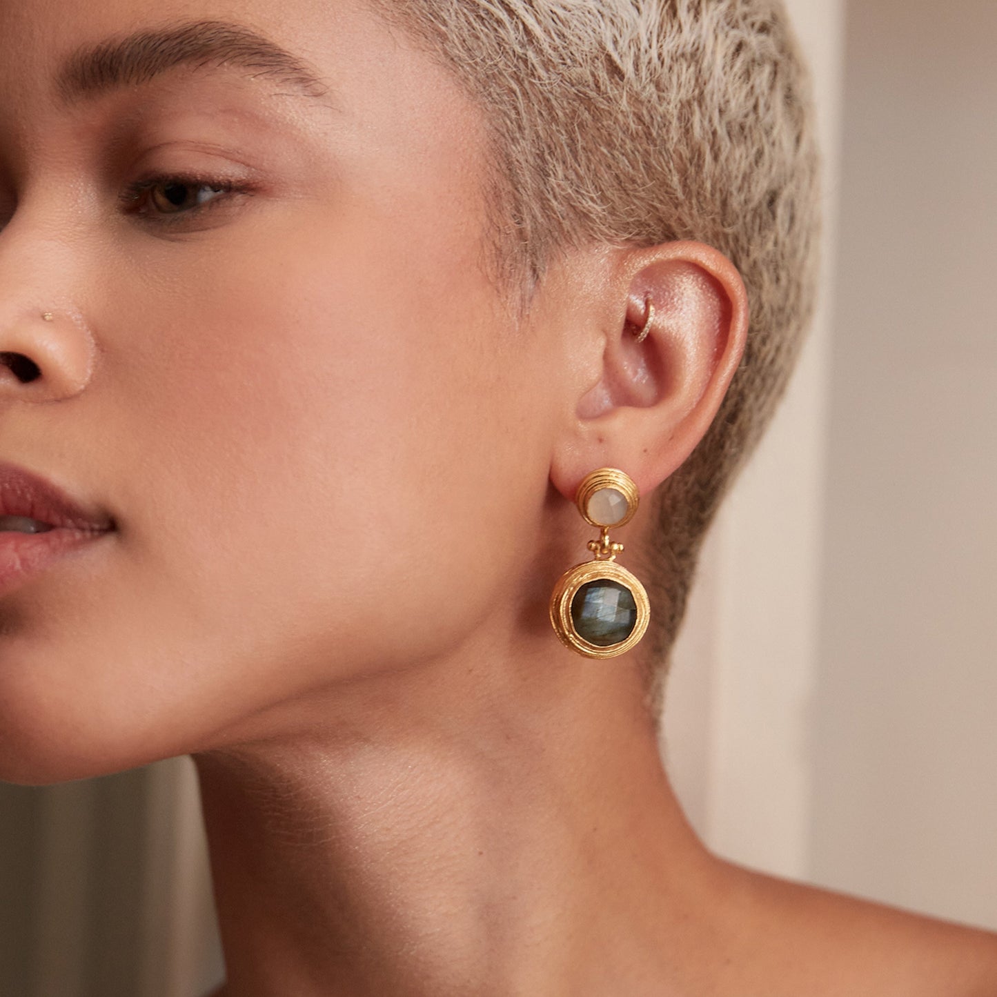 Close-up of a woman wearing gold earrings with a neutral background