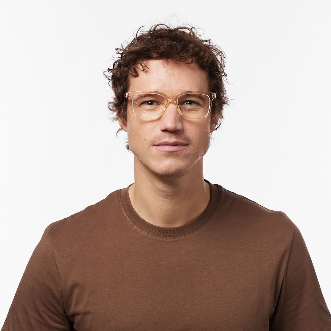 Man wearing reading glasses and a brown t-shirt against a white background
