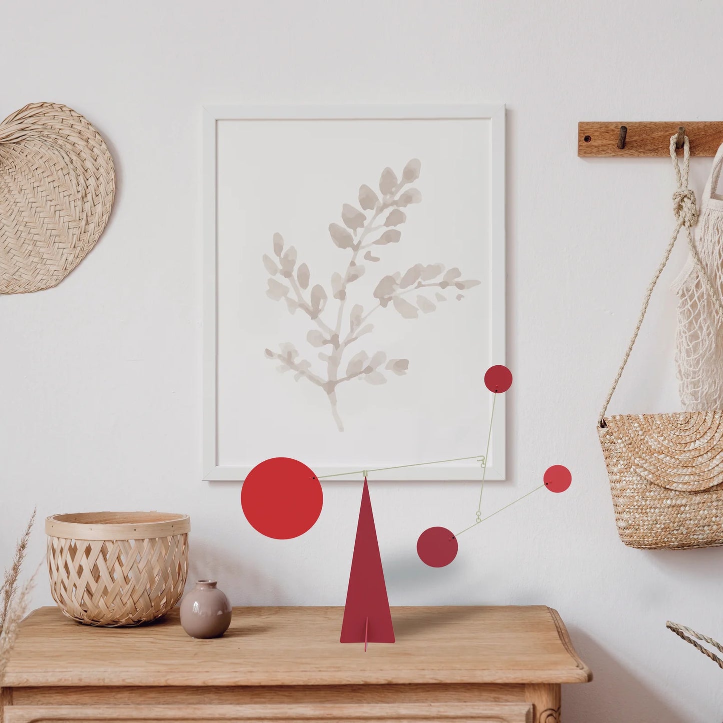 Decorative elements on a wall with a framed artwork, red circular standing mobile, and a woven basket.