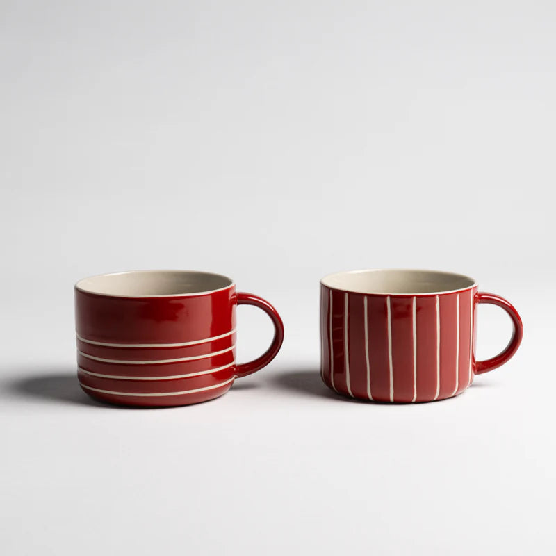 Two red ceramic mugs with white stripes on a light gray background